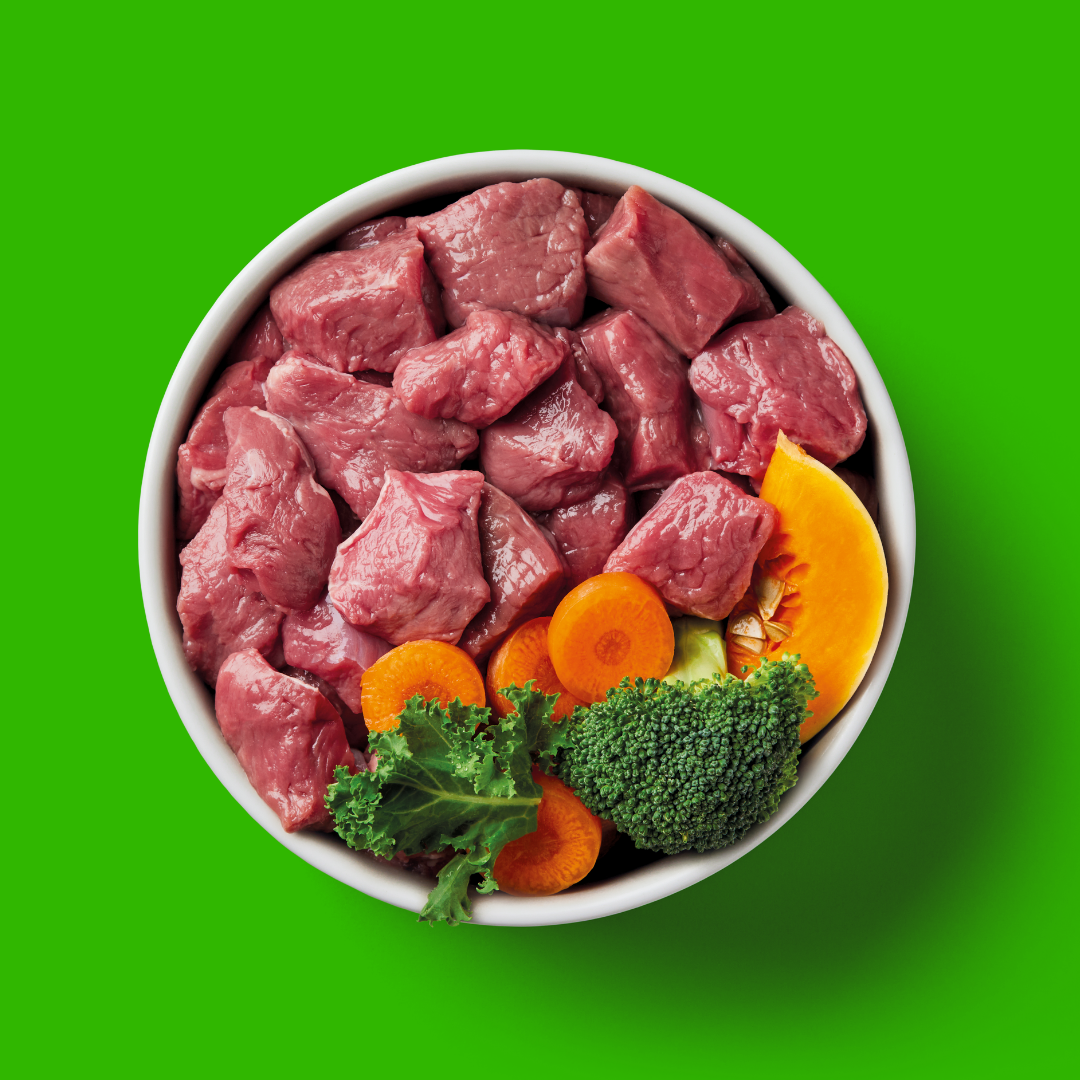 Raw beef chunks with vegetables in a bowl on a green background