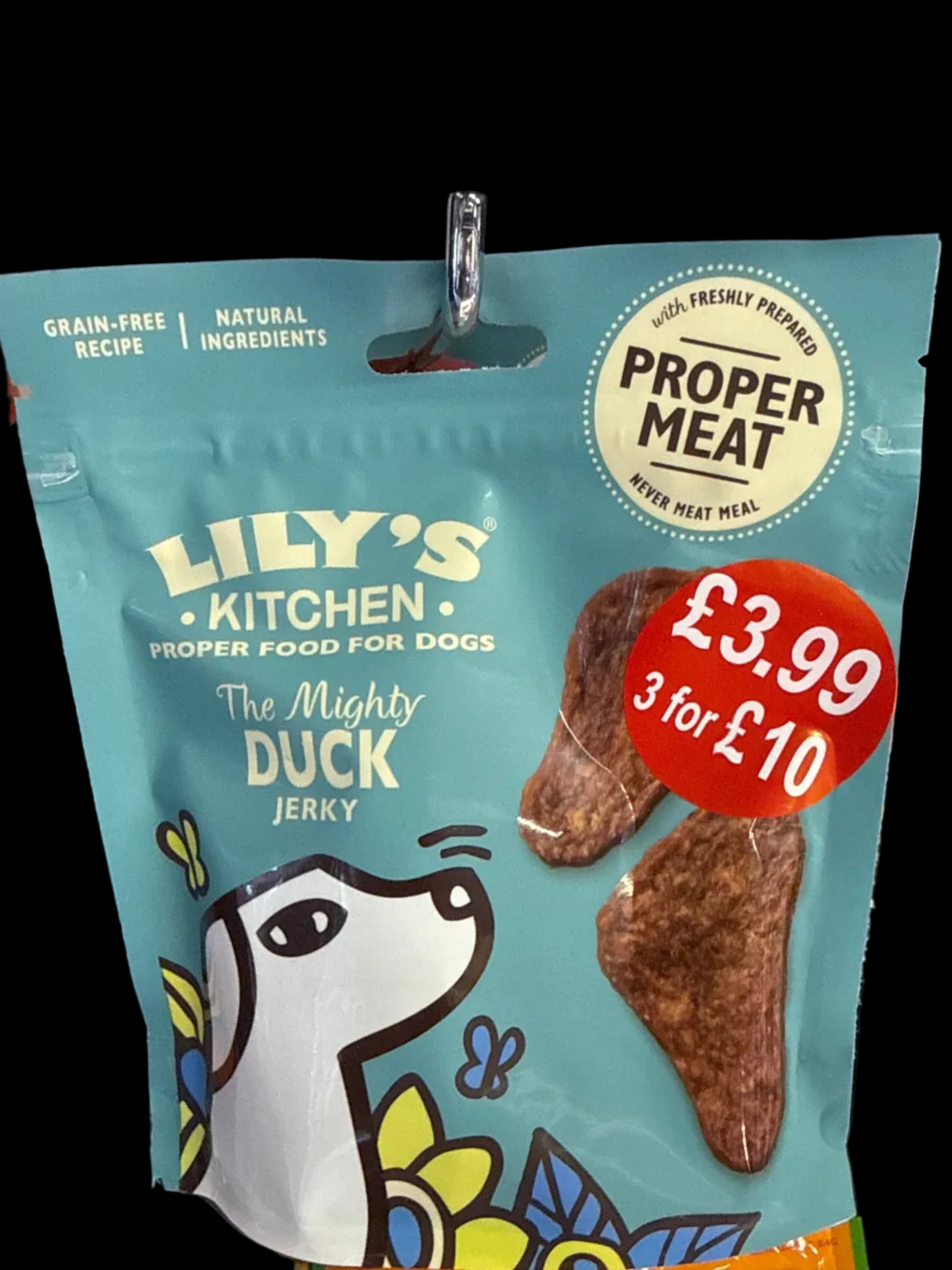 A bag of Lily's Kitchen 'The Mighty Duck Jerky' dog treats on a store shelf. The packaging is light blue with a cartoon duck illustration, a red price sticker showing '3 for £10', and a white 'Proper Meat' seal.