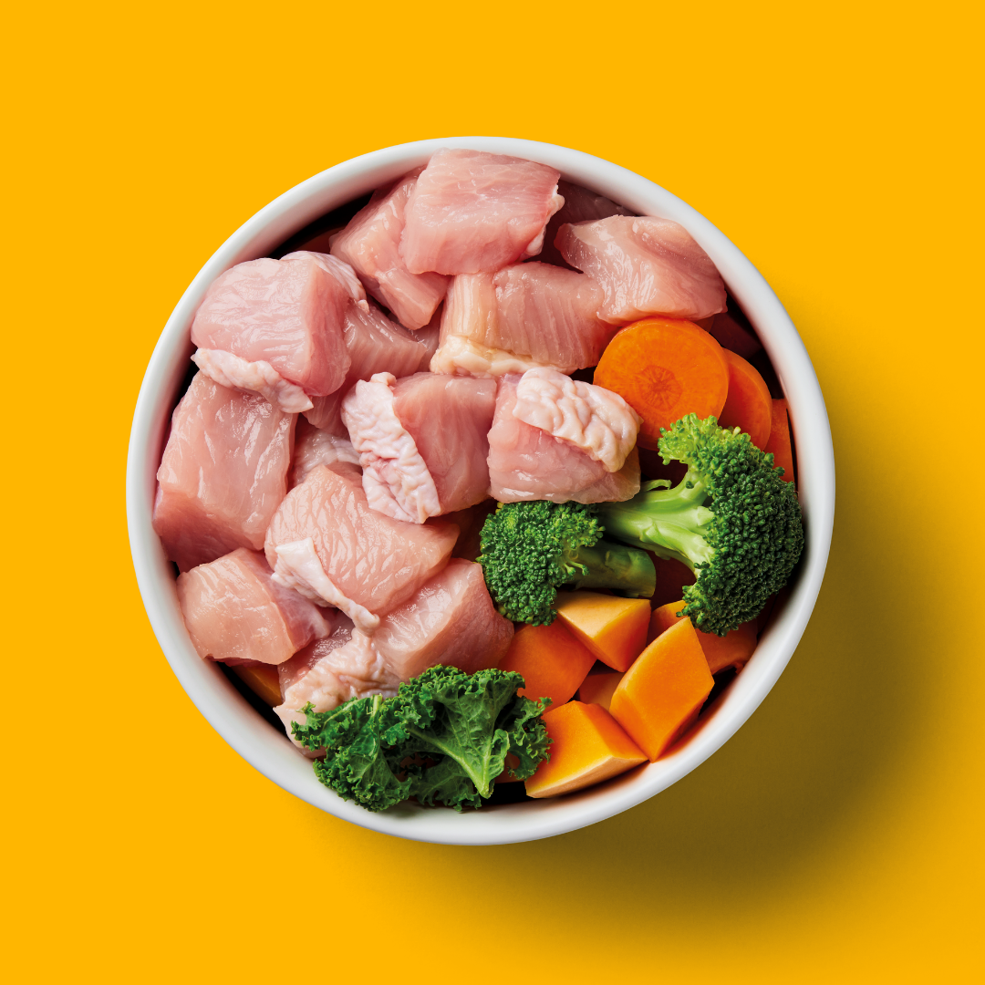 Raw chicken pieces with vegetables in a bowl on a yellow background